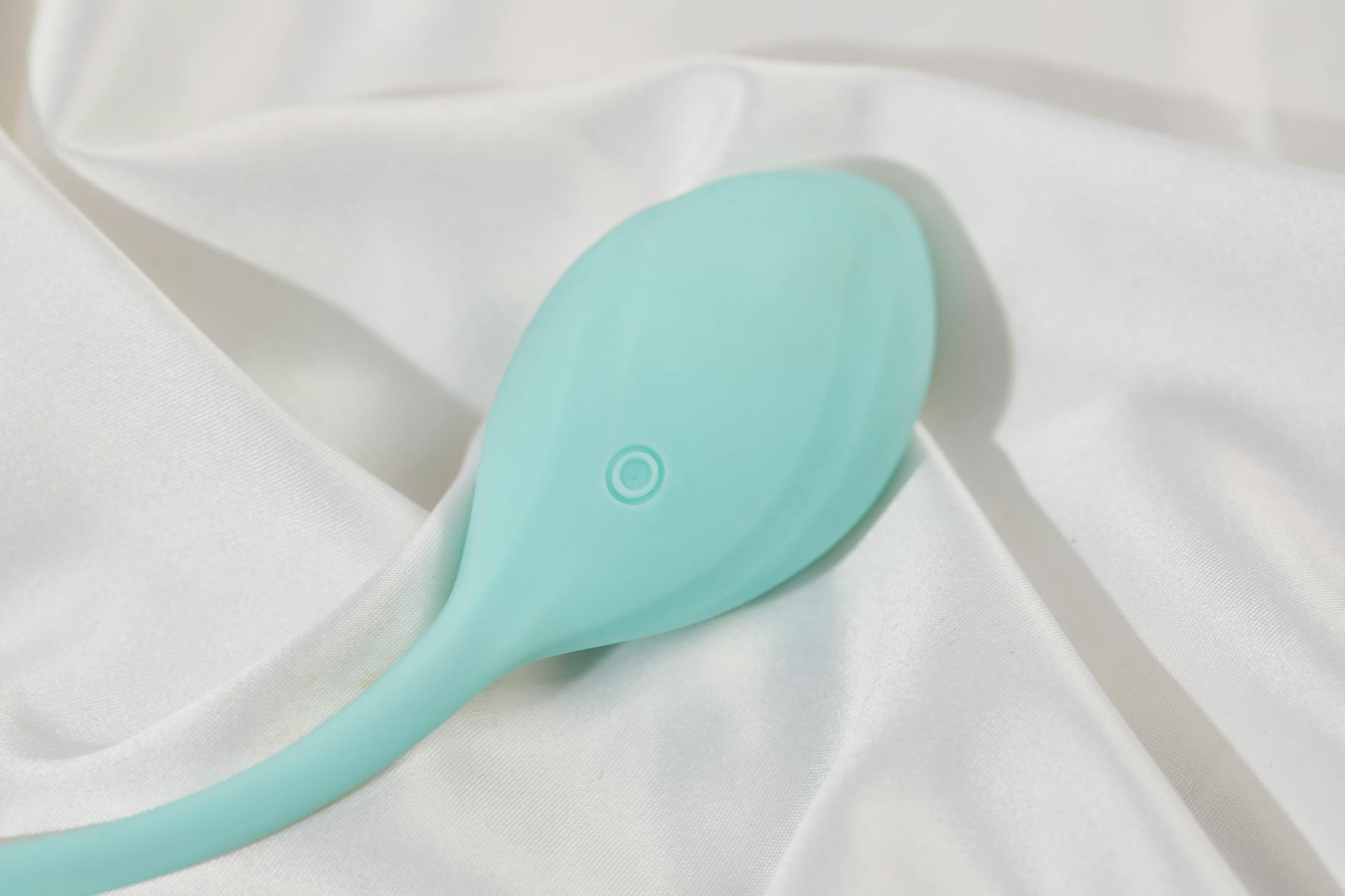 A stylish teal vibrator on smooth white silk fabric