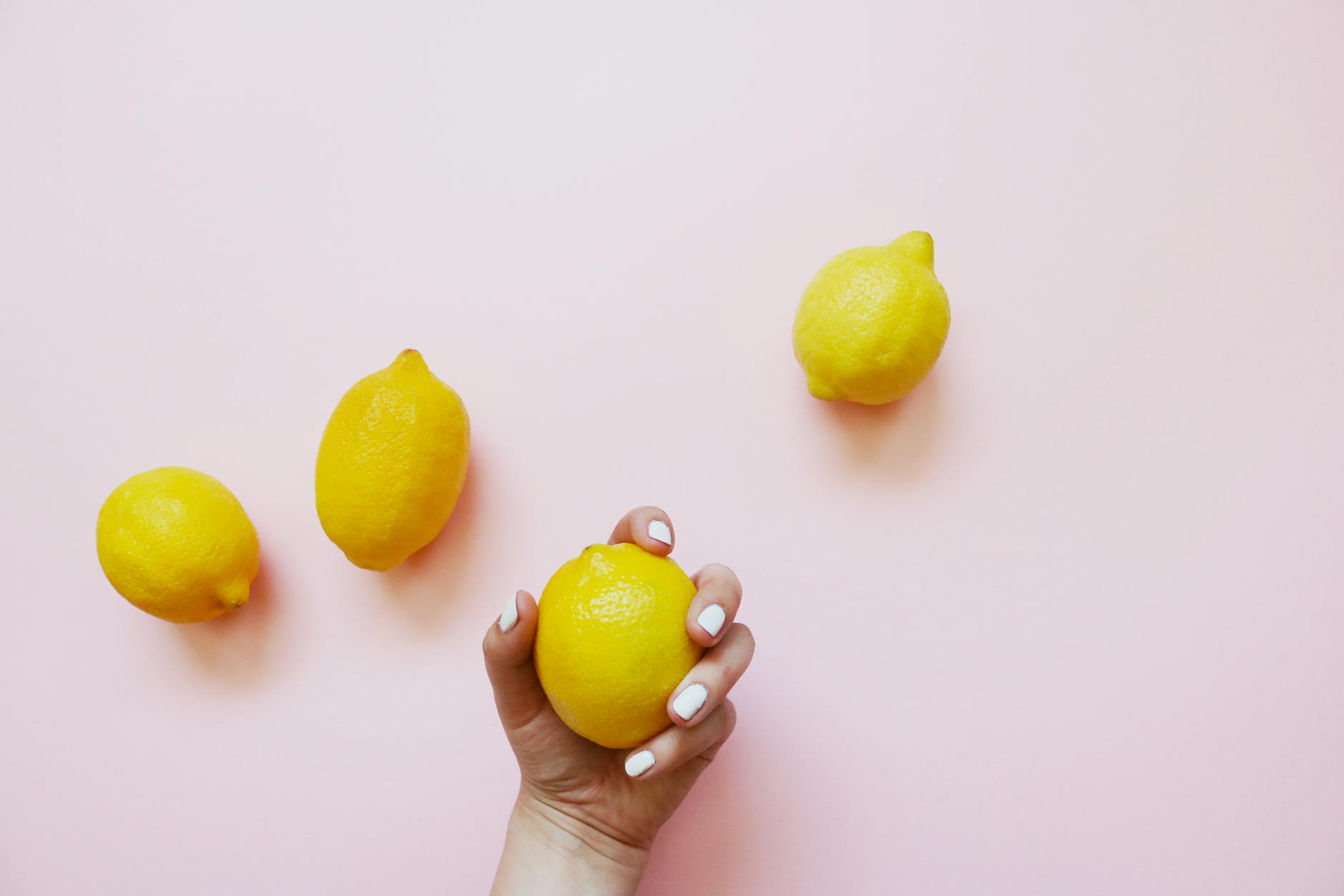 A hand holding a fresh lemon on a soft pink background, symbolizing the cyclical nature of pleasure and sensation