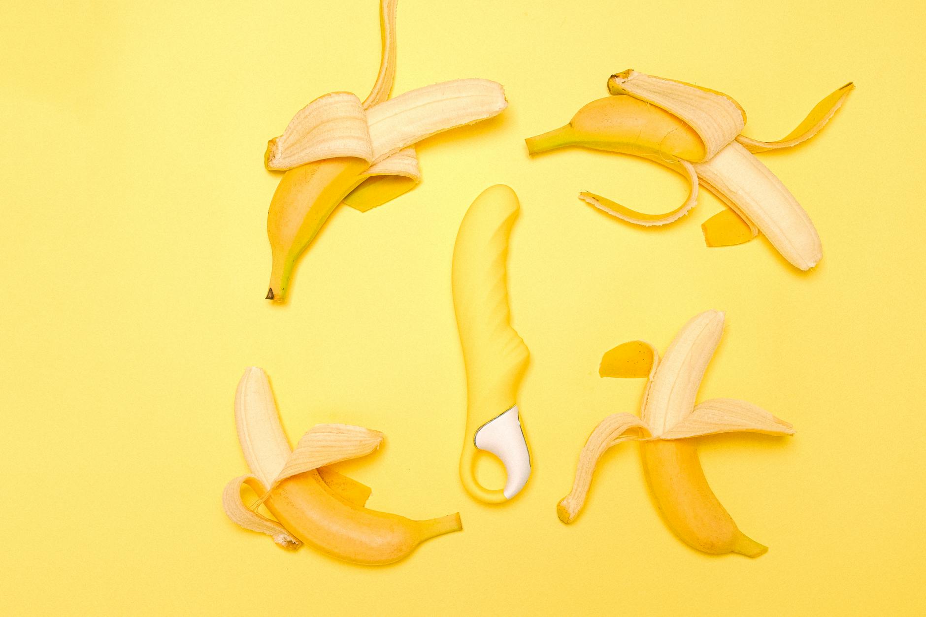 A lemon clitoral vibrator surrounded by fresh citrus on a bright yellow surface