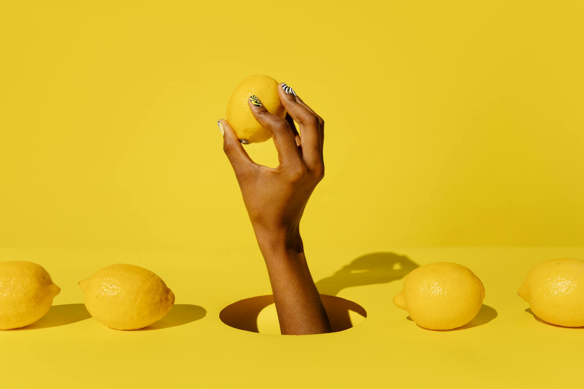 Hand holding a fresh lemon against a vibrant yellow background, representing intimacy and freshness.