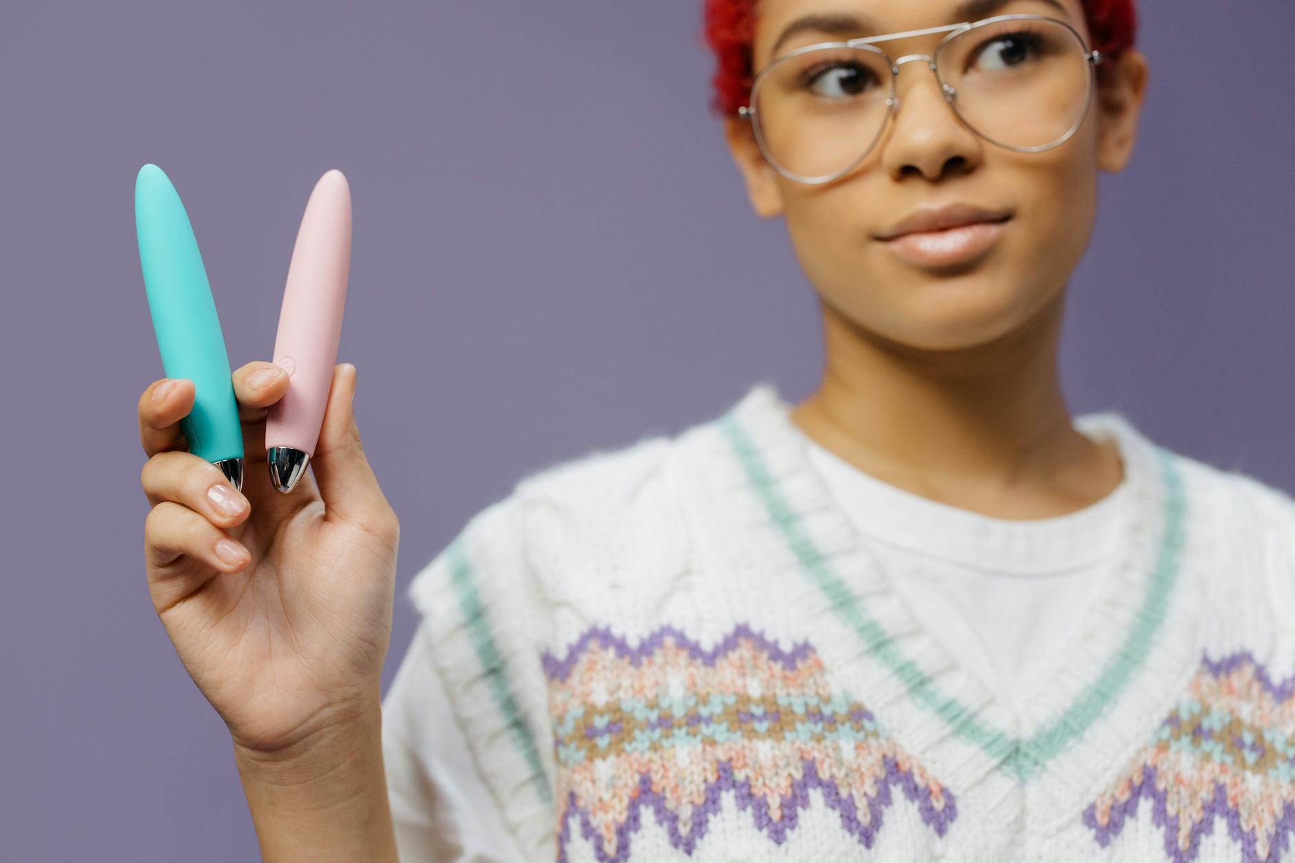 Woman holding two colorful vibrators against a purple background, representing options for sexual wellness.