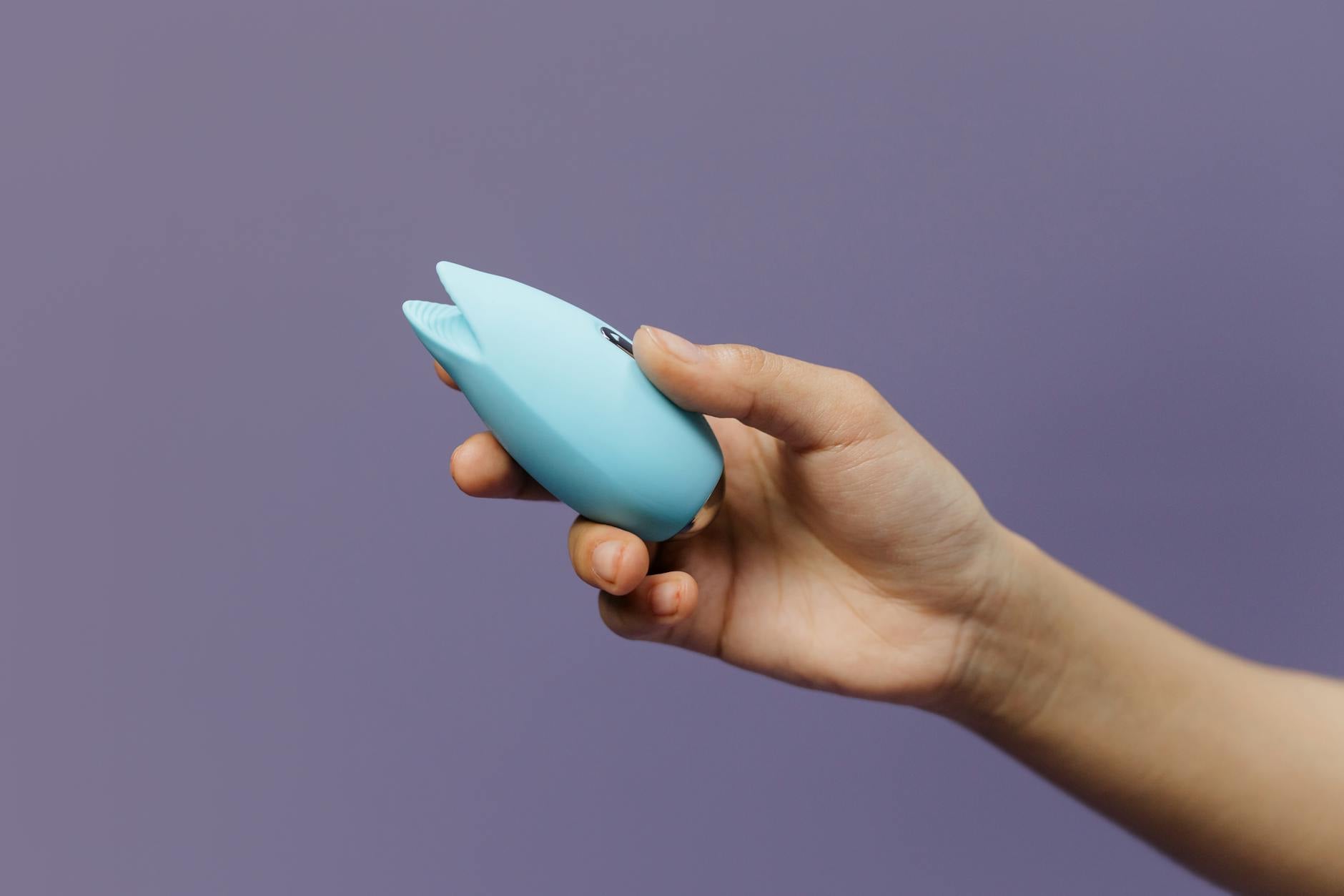 A blue silicone lemon vibrator held in hand against a solid purple background
