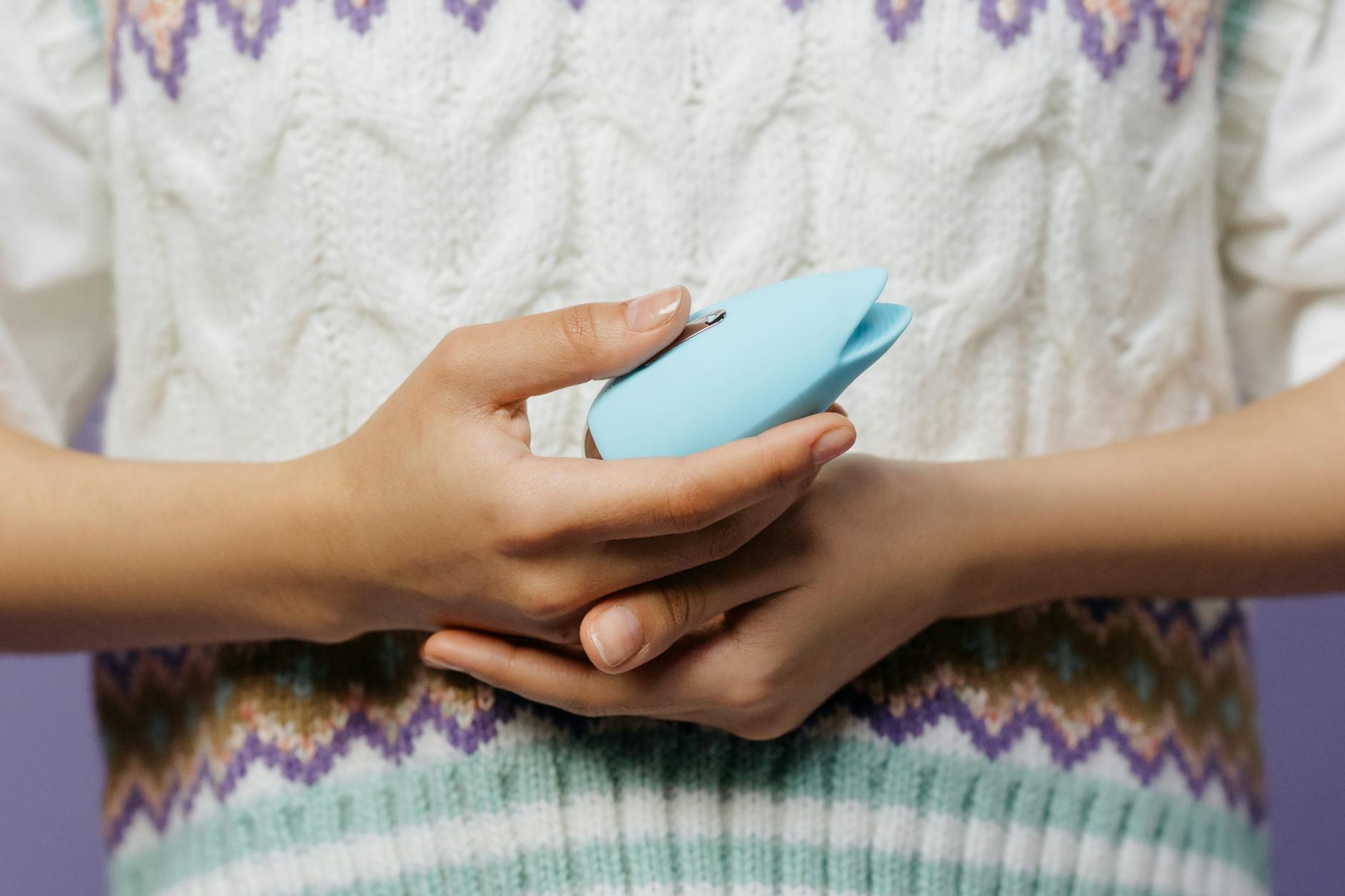 Close-up of hands holding a lemon vibrator against a knitted sweater in natural light